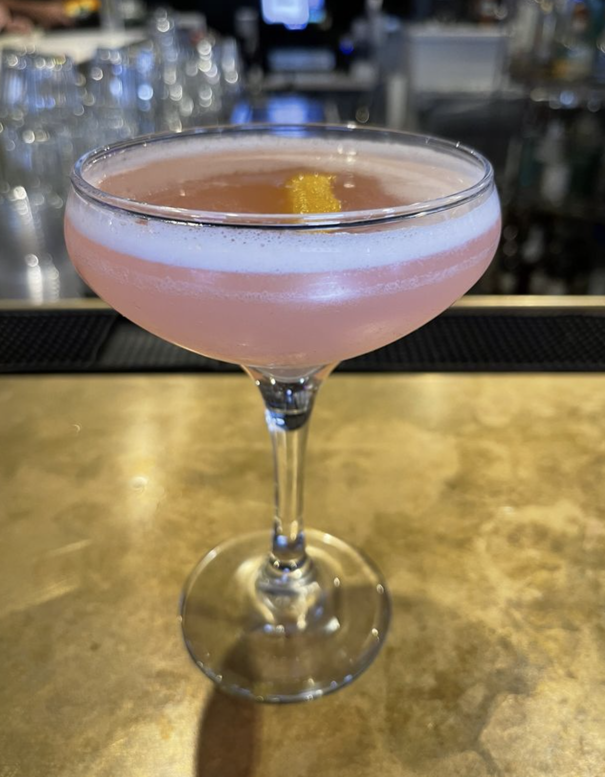 A pink cocktail in a coupe glass on the brass bar top at Savoy Tivoli